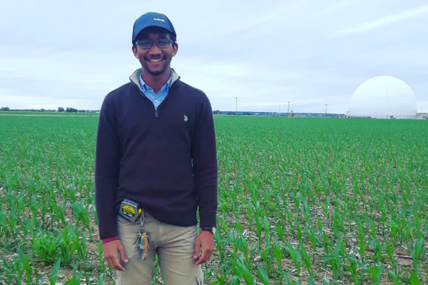 man wearing hat and glasses standing in crop field