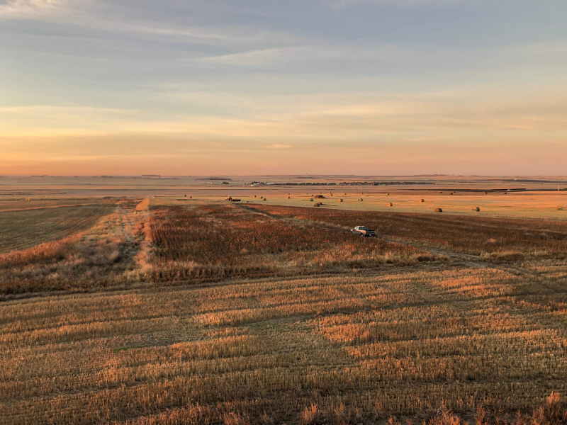 aerial view of sunrise over farm field with truck, hay bales, and crops