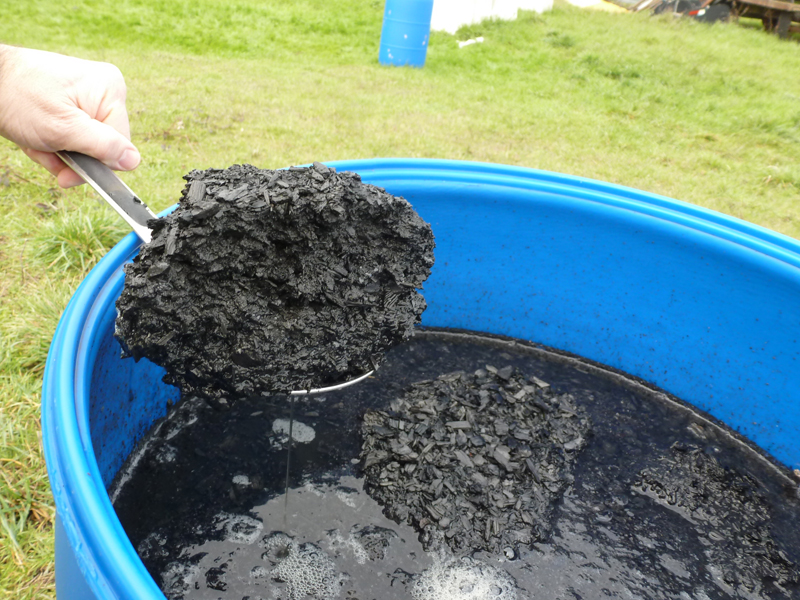 Scoop of biochar from tub of liquid