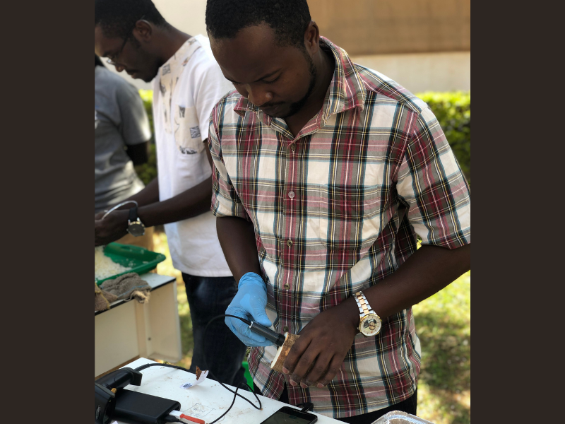 man wearing watch and glove using handheld spectrometer connected to smartphone on cassava crop